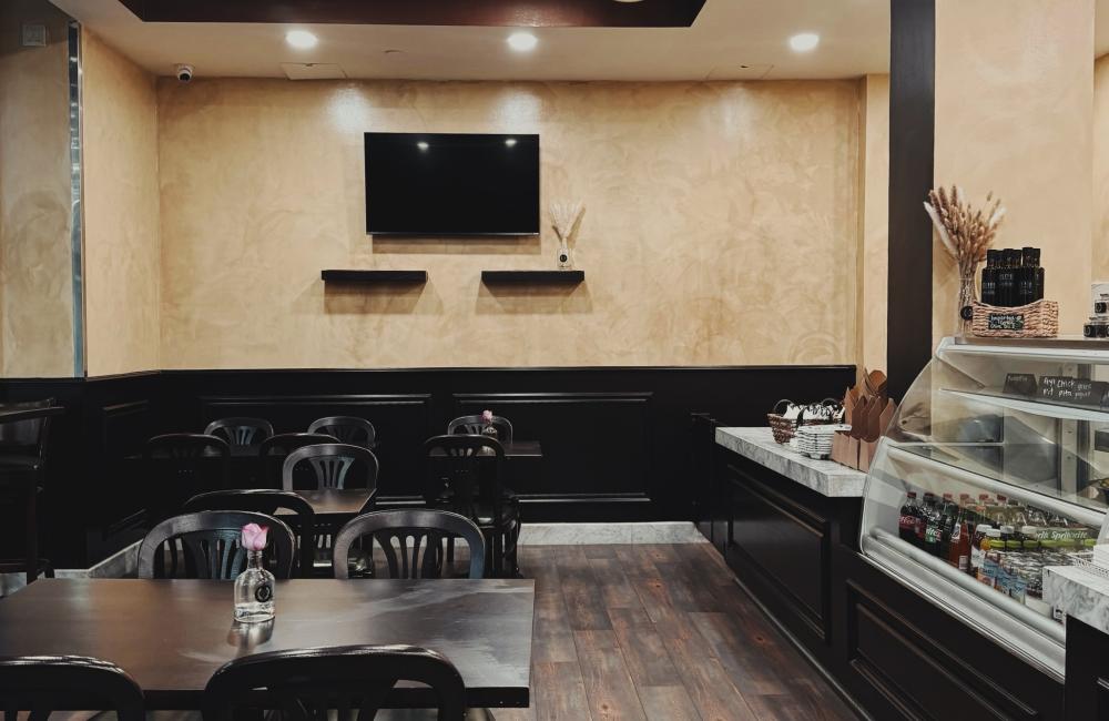 A small café dining area with black chairs, a vase with a pink flower, and a refrigerated drink display.