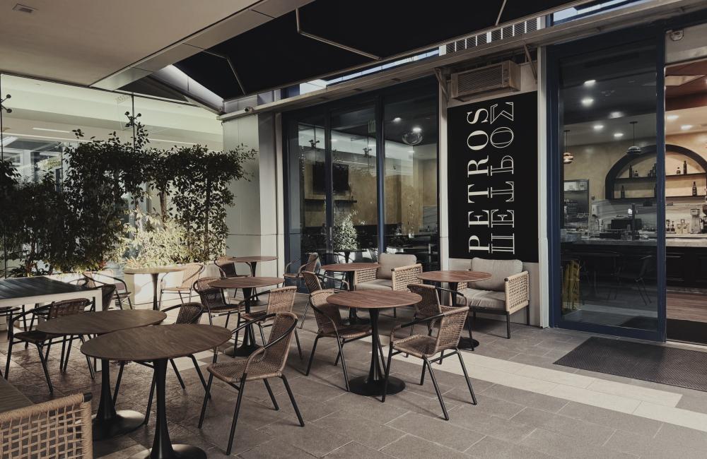 Outdoor café seating with empty wicker chairs and round wooden tables under an awning.