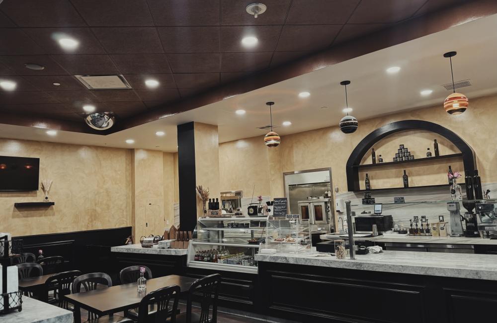 A cafe interior featuring marble countertops, display case with drinks, and tables with single pink flowers.