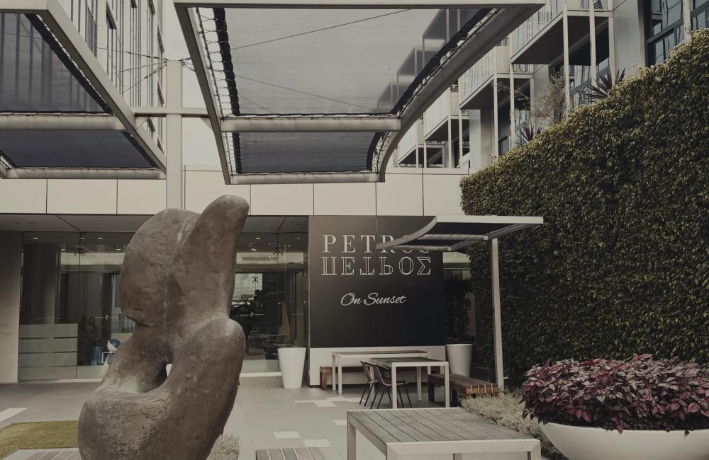Abstract stone sculpture stands on a pedestal in an outdoor courtyard with benches, tables, and plants.