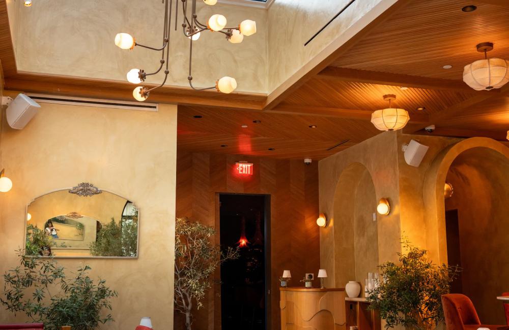 A quiet restaurant interior with red chairs, marble tables, and a large chandelier under a glass ceiling.