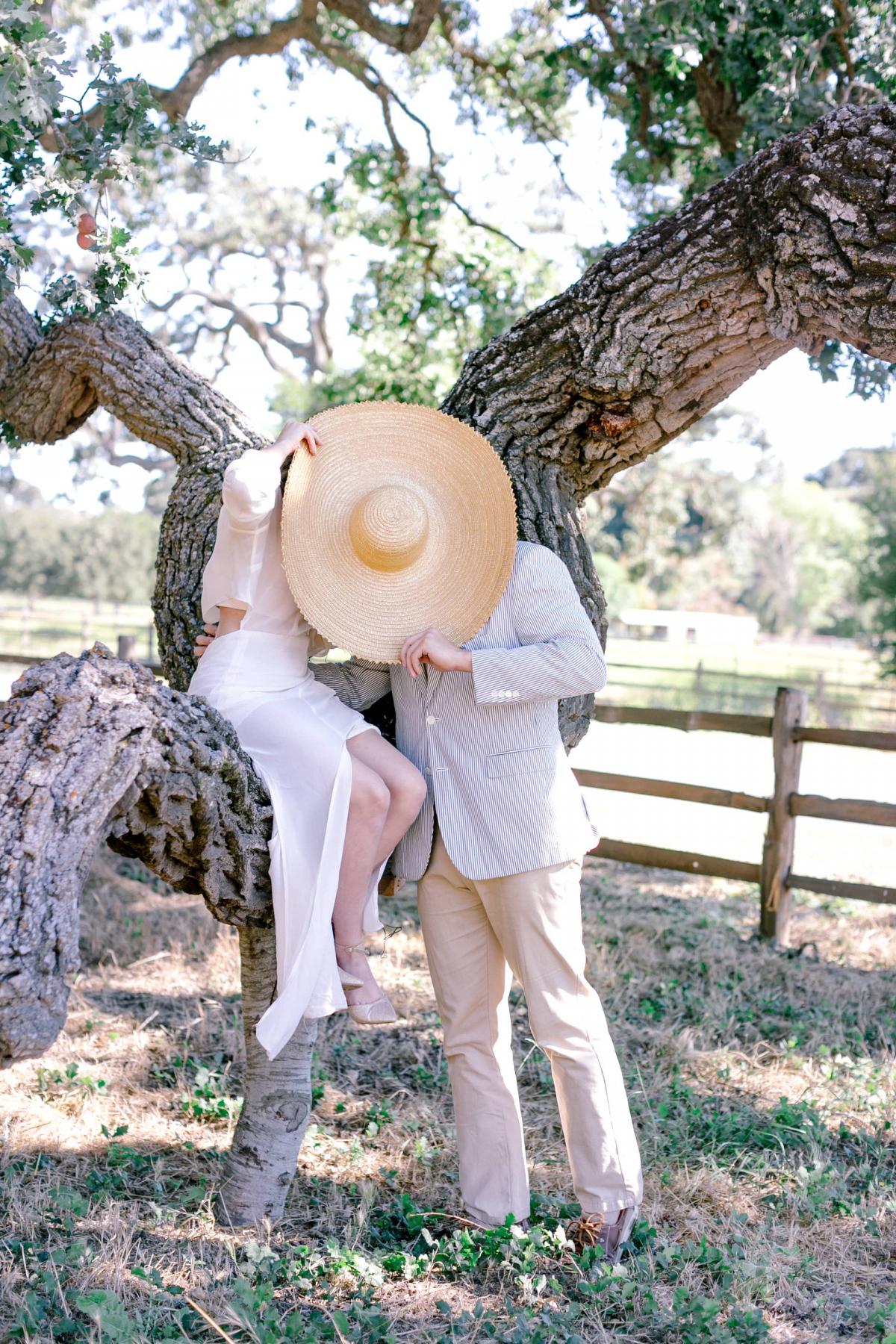 Bride & Groom Sitting on Tree Branch While Hiding Behind Hat for Mika & James's Wedding