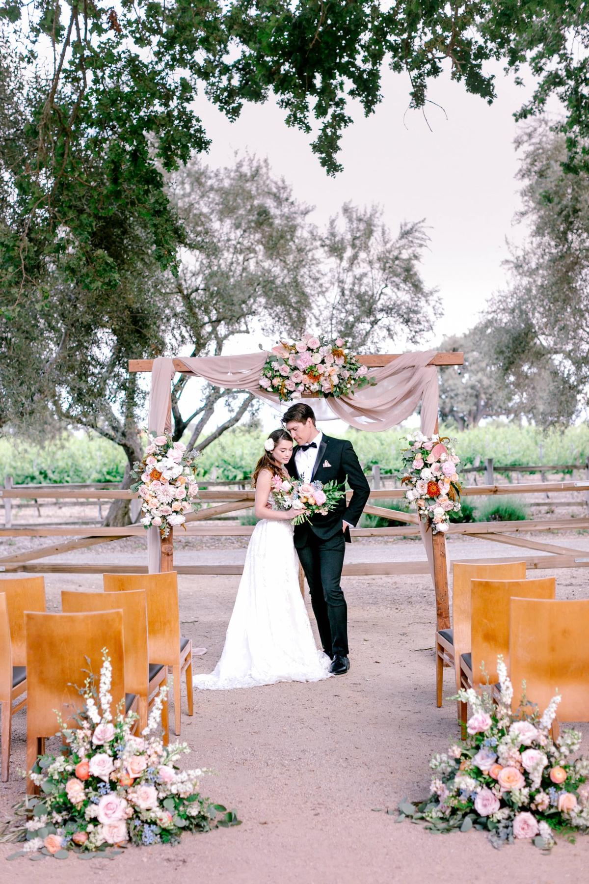 Outdoor Reception Area with Chairs, Flower Arrangements with Bride & Groom Under Archway for Mika & James's Wedding