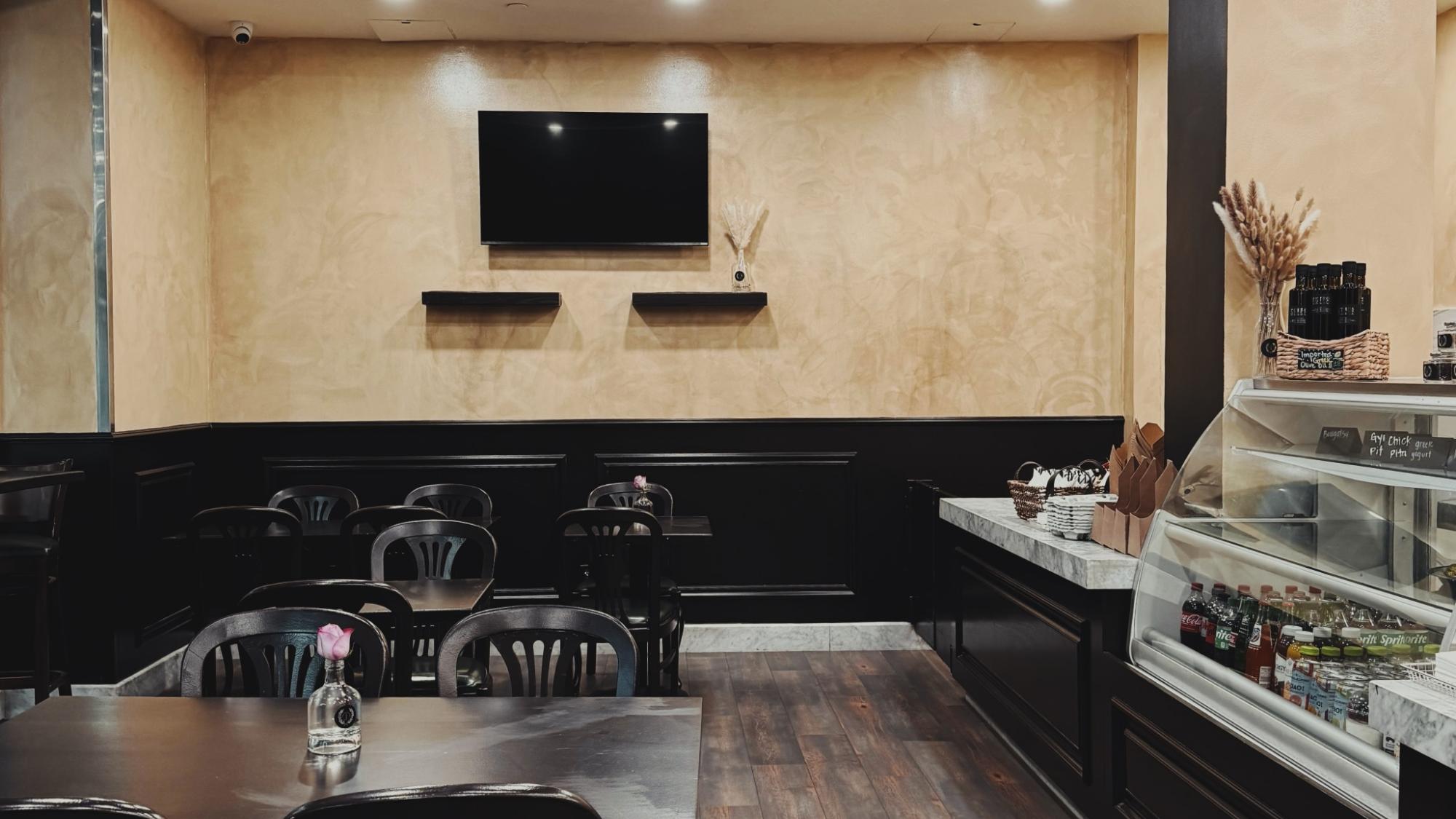 A small café dining area with black chairs, a vase with a pink flower, and a refrigerated drink display.