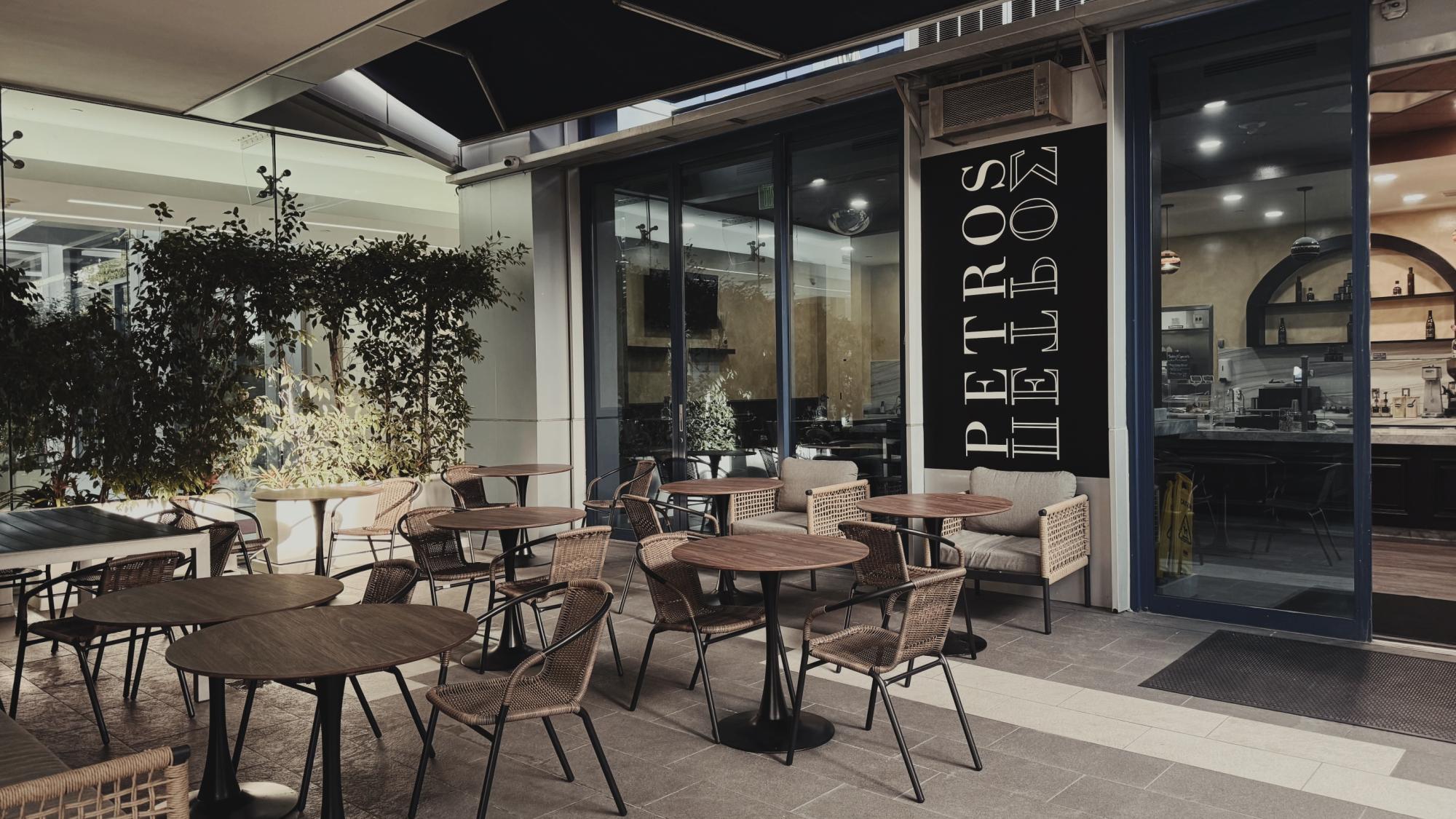 Outdoor café seating with empty wicker chairs and round wooden tables under an awning.
