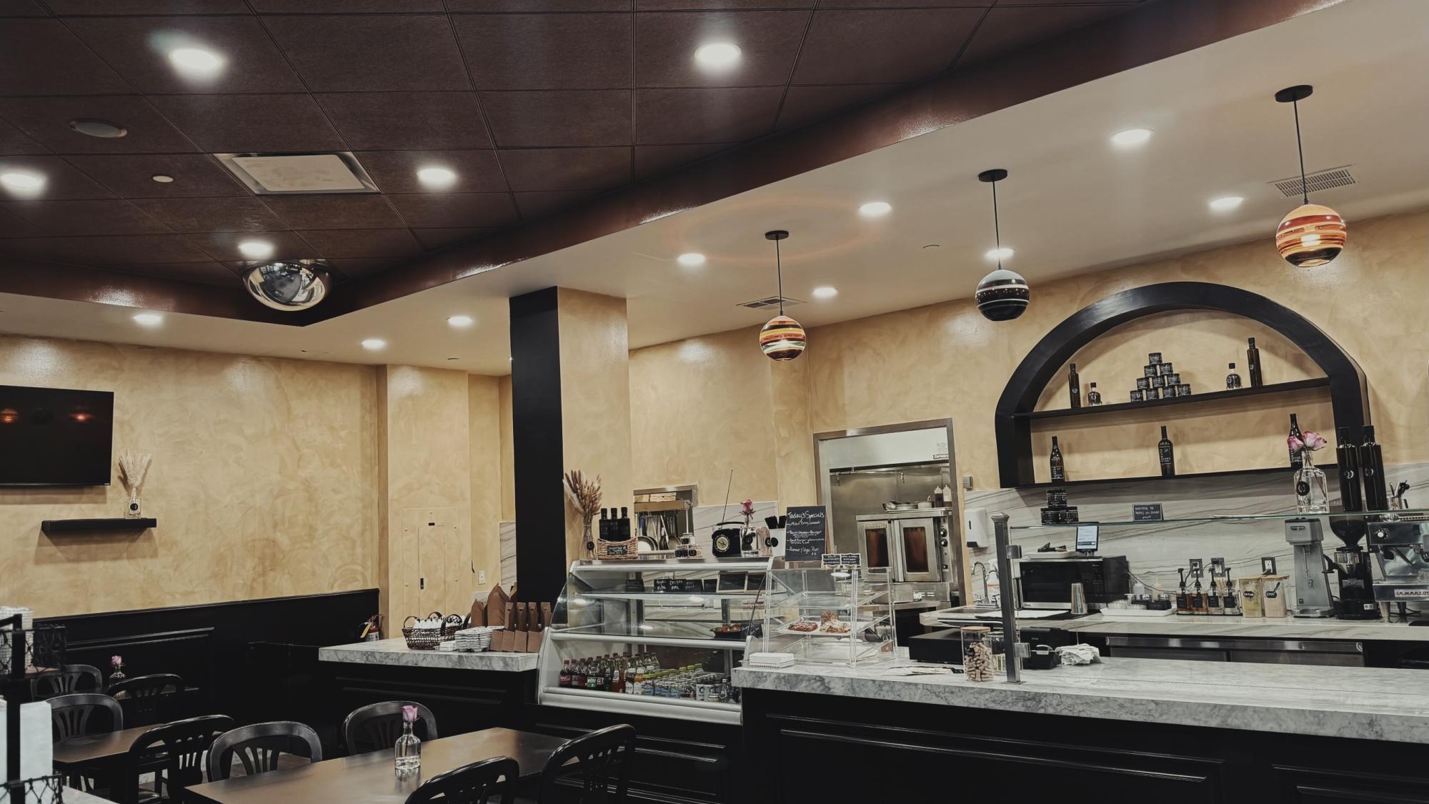 A cafe interior featuring marble countertops, display case with drinks, and tables with single pink flowers.