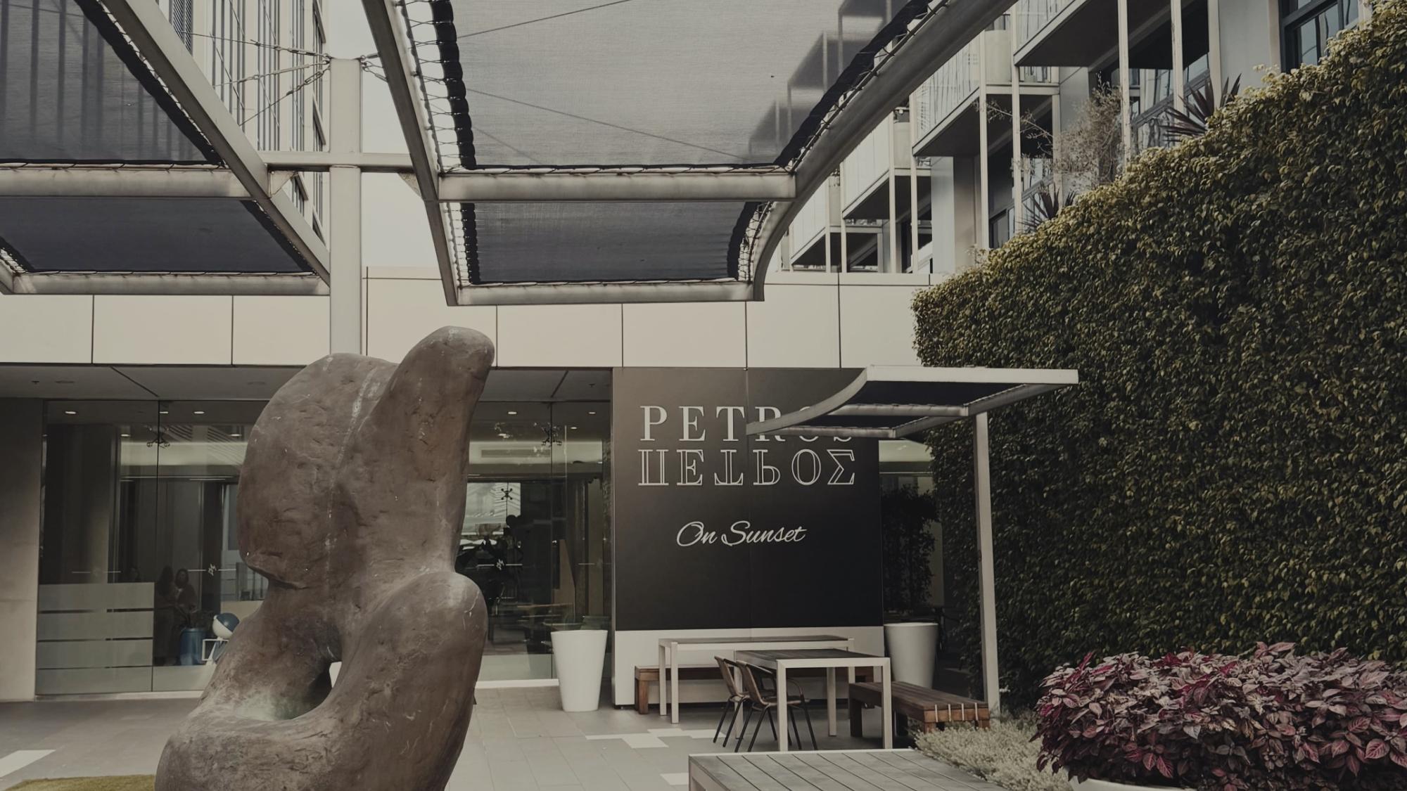 Abstract stone sculpture stands on a pedestal in an outdoor courtyard with benches, tables, and plants.